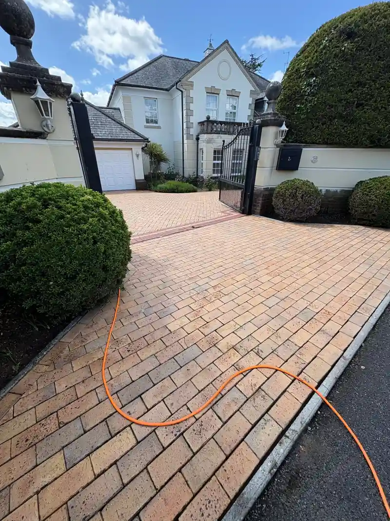 A block paved drive part way through being jet washed, with our hose across it