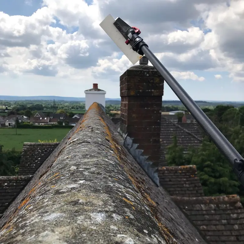 Cleaning a roof ridge with a long brush, high above the rooftops
