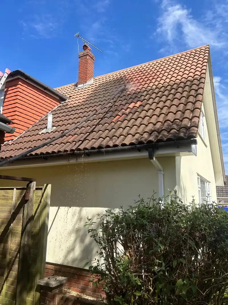 A tiled roof part way through cleaning, with a cleaning pole on the tiles