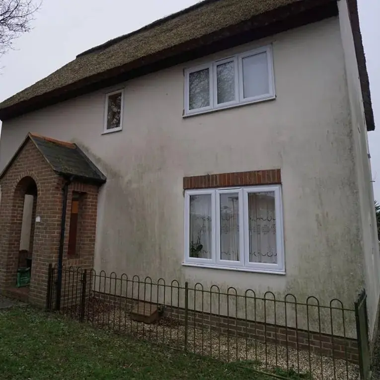 A cream rendered house before cleaning, with grey, stained walls